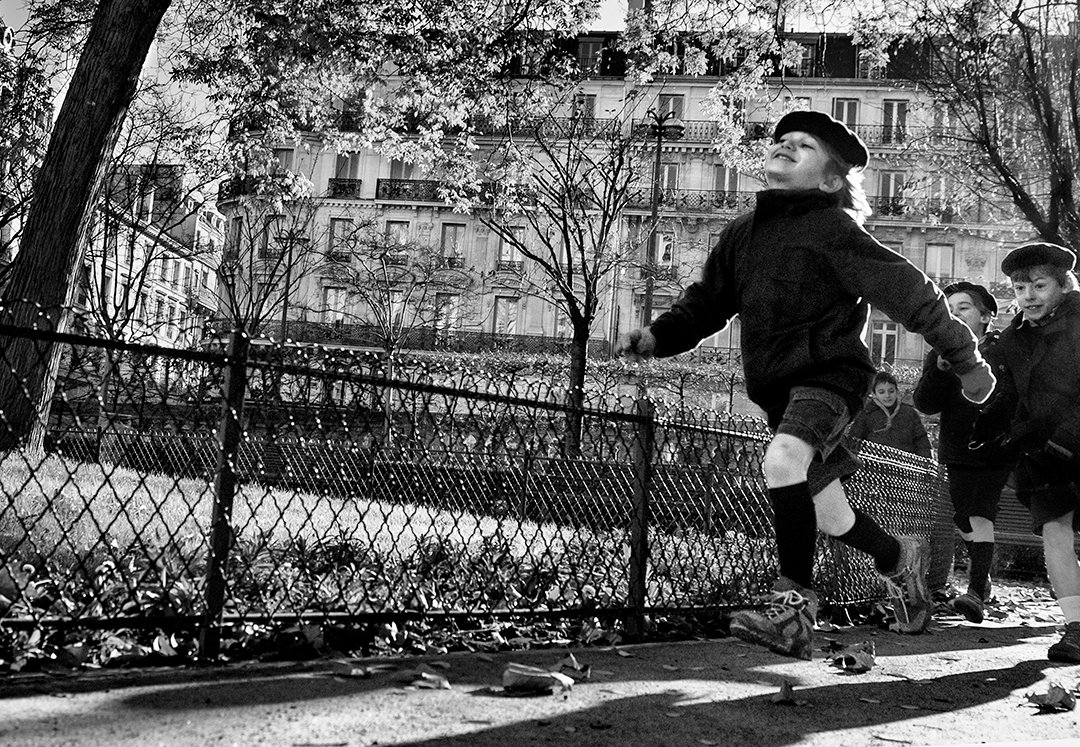 Children running beside a fence and a tree.